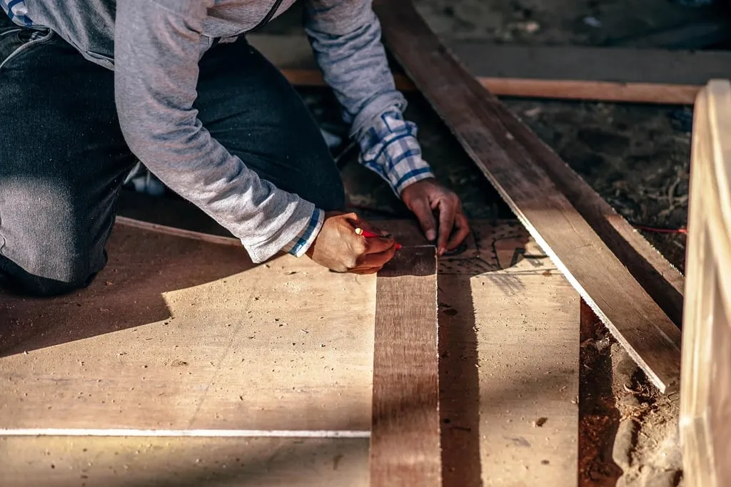 Close-up of a carpenter's hands marking a wooden plank with a pencil in warm light