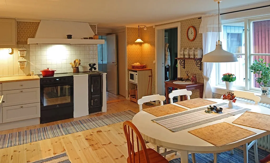 Farmhouse kitchen with rag rugs on a pine floor and a white round table and chairs by a sunny window
